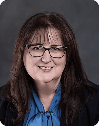 Professional woman wearing glasses and a blue blouse, smiling for a corporate headshot.