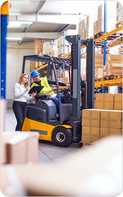 A forklift operator and supervisor inspecting inventory in a warehouse.