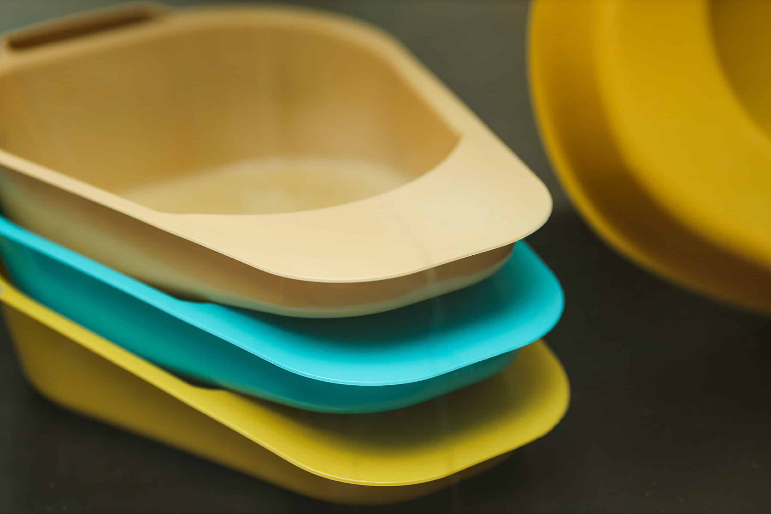 Disposable hospital trays in beige, teal, and yellow for medical use.