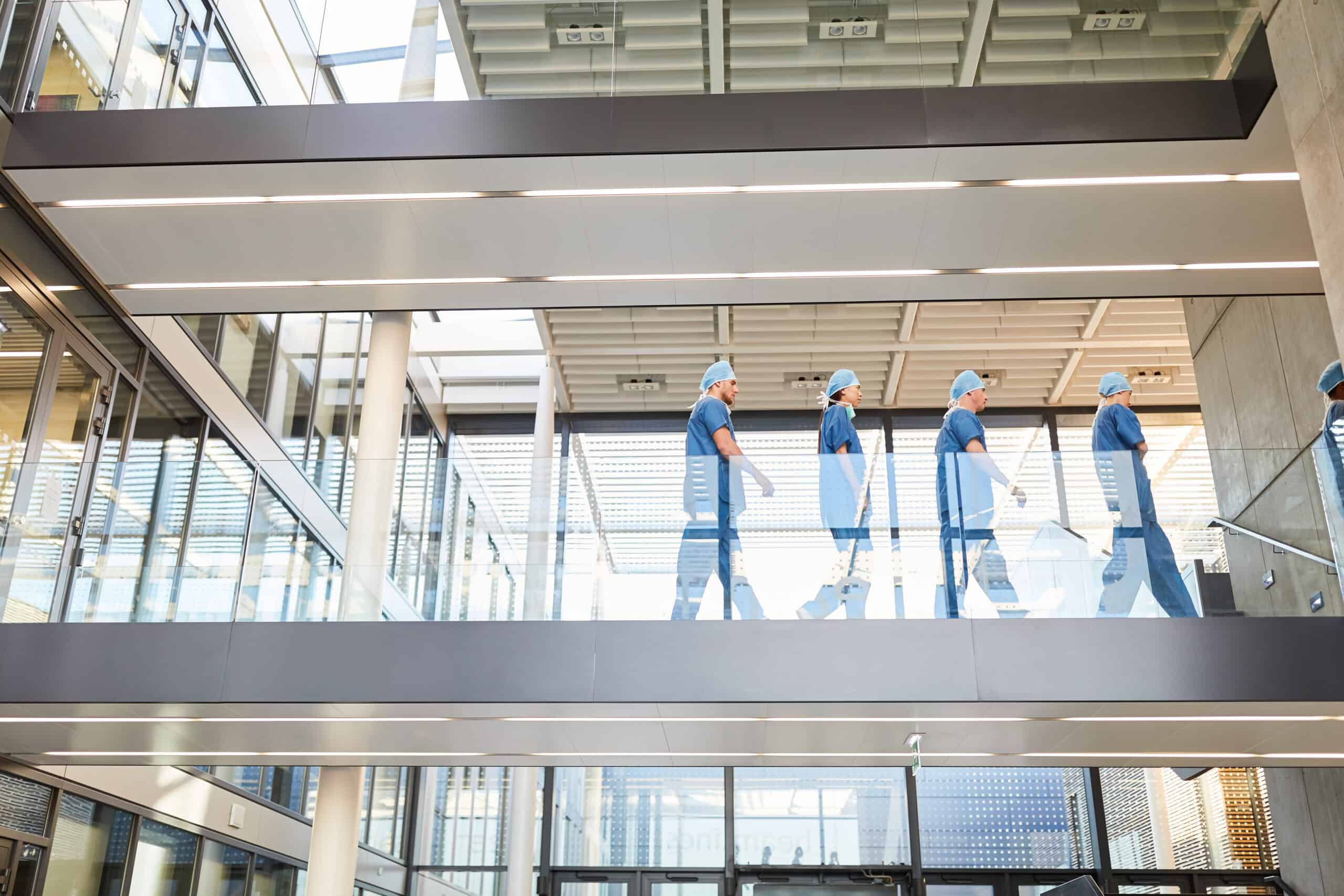 Medical staff in scrubs and masks walking in hospital corridor.