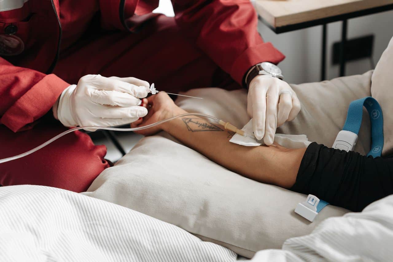 Medical professional drawing blood from patient’s arm in hospital setting.