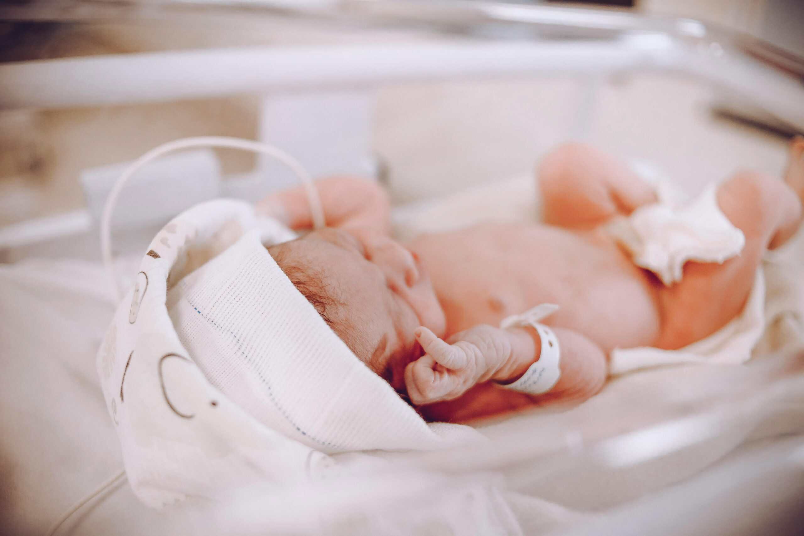 Premature newborn baby in neonatal incubator at hospital.