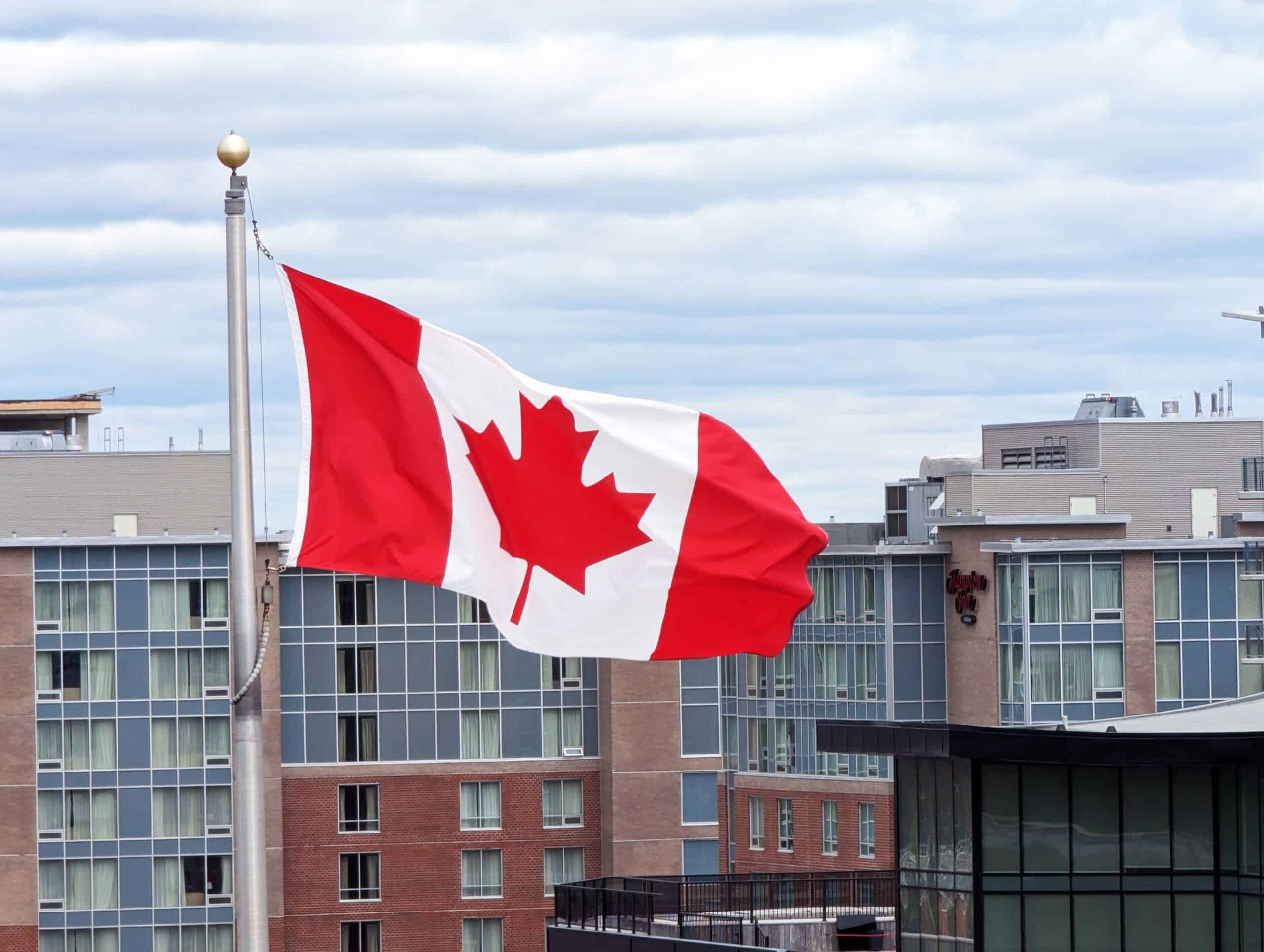 Canadian flag flying in front of modern urban buildings.